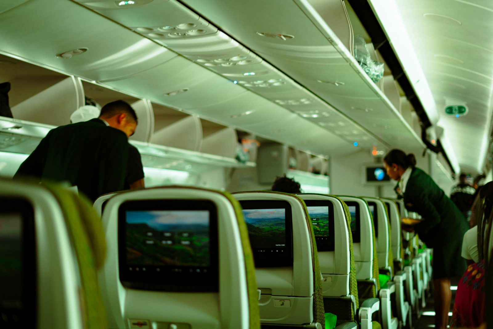 Cabin crew serving passengers on both sides of the aisle, seen from a passenger seat